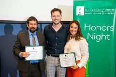 Three smiling people, two holding awards certificates, standing next to a green banner with white text reading The University of Vermont Larner College of Medicine, Honors Night.