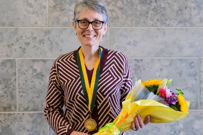 Dr. Anne Dixon, wearing an investiture medallion and holding a bouquet of flowers