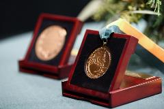 Two medallions displayed in wooden boxes, one is hanging on a green and gold ribbon.