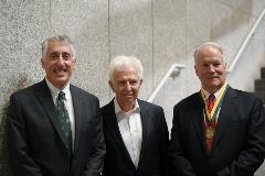Three men stand together, one wears a medallion on green and gold ribbon.