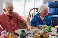 Two people seated at a table, smiling, with plates and coffee cups before them.