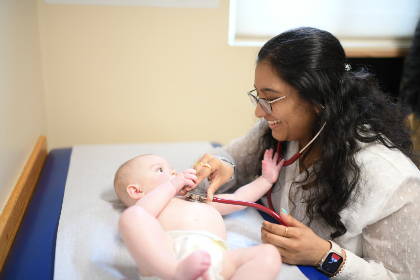 A medical student smiling while listening through a stethoscope positioned on the baby's chest